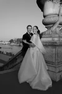 Black and white portrait of the groom embracing the bride while she looks toward the sky and laughs on the Pont Alexandre III bridge.
