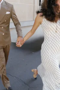 Bride in a white polka-dot dress running hand in hand with the groom in a brown suit during their engagement session in Paris.