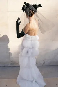 Bride posing against a Paris stone wall in a couture gown with layered silk texture, black gloves, and a veil headpiece.