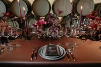 Refined rehearsal dinner place setting with burgundy florals, candles, and layered dinnerware designed for an intimate winery celebration.