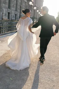 Bride and groom running together near historic Paris architecture and lantern-lined streets as the bride’s flowing gown moves in the wind.