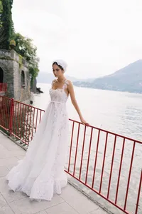 Model in textured lace gown standing by red railing at Villa Cipressi with the background of Lake Como