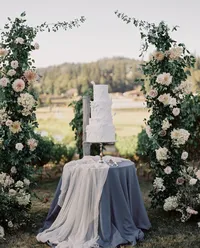 Elegant wedding cake displayed on a silver tray with dusty blue linen and silk overlay surrounded by romantic garden florals during a Lake Oswego Oregon winery wedding.