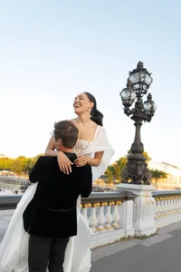 Groom lifting the bride and spinning her on the Pont Alexandre III bridge as they laugh together.