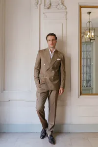 Portrait of the groom indoors in Paris wearing a brown suit with a mirror reflecting the interior behind him.