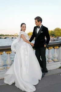 Bride standing on the Pont Alexandre III bridge in a flowing silk gown while the groom looks toward her.