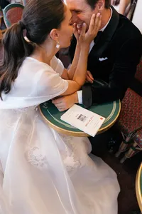 Close portrait of the bride holding the groom’s face as they laugh together at their table at Café de Flore in Paris.
