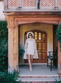 Bride in a cream coat and heels walking past a carved wooden door at a Santa Barbara estate, from a wedding editorial by Yuliya Supin Design