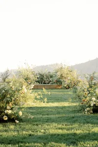 Ceremony setup featuring a pedestal altar and tall organic floral arch framed by wild yellow blooms and open Oregon valley sky.