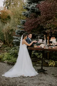 Bride and groom cutting cake at outdoor wedding reception table in garden setting