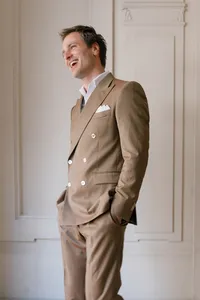 Portrait of the groom standing indoors in Paris wearing a brown suit, smiling with his hands in his pockets during the engagement session.