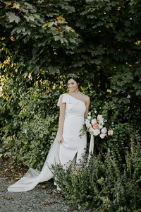 Bride standing with bouquet against lush greenery in outdoor wedding setting