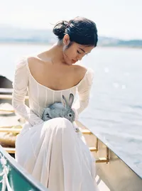 Bridal editorial portrait in canoe holding rabbit on water in natural setting