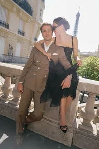 Bride and groom seated together on a stone fence during their Paris engagement session with the Eiffel Tower behind them.