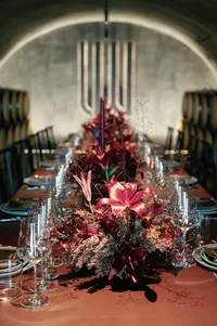 Long table rehearsal dinner design inside a winery cellar surrounded by oak barrels and candlelit floral arrangements.