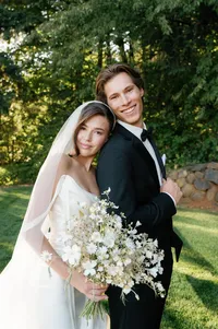 Bride embracing groom from behind with white bouquet as they laugh together before ceremony.