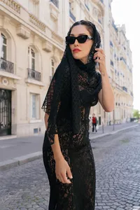Portrait of the bride standing in the middle of a Paris street wearing a black lace dress, silk scarf, glasses, and red lipstick.