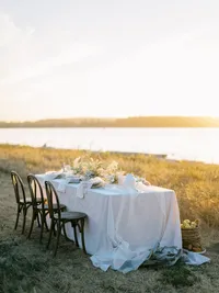 Outdoor wedding table at sunset by water with soft linen and natural design