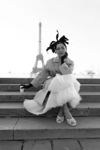 Bride sitting on steps in Paris wearing a trench coat over a couture gown with the Eiffel Tower in the background.