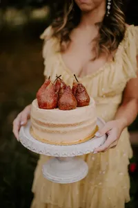 Wedding cake topped with poached pears held by guest in outdoor reception setting