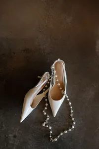 Bridal morning accessories including Chanel necklace and heels styled on canvas backdrop.