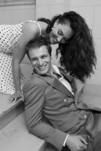 Bride and groom laughing together on a staircase in Paris as the groom sits while the bride leans toward him from behind during their engagement session.