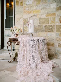 Wedding cake table styled with candles, florals and silk linen at Sunstone Winery stone entrance in Santa Ynez Valley.