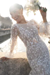 Bride laughing while holding her bouquet on a Paris bridge with the Seine River behind her.