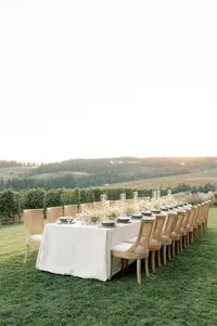 Long outdoor dinner table set in an open Oregon vineyard field at golden hour