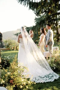 Bride walking toward ceremony aisle lined with florals as guests applaud at Lucid Wild Vineyard.