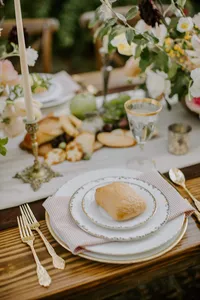 Outdoor wedding table setting with layered plates, bread, and gold flatware