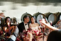 Bride and groom seated during an intimate rehearsal dinner in a winery cellar surrounded by candlelight and guests.