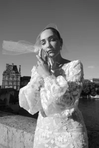 Black and white fashion portrait of the bride holding her veil as it moves in the air along the Seine River in Paris.