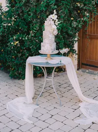 Flowing chiffon draping the base of the cake table on a stone terrace, a styling detail from a Santa Barbara wedding editorial by Yuliya Supin Design