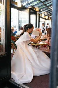 Bride sitting at Café de Flore in Paris laughing as she playfully hides her face behind the menu while waiting for the groom.