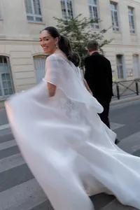 Bride running playfully through a Paris street with her gown moving in the wind as the groom follows beside her.