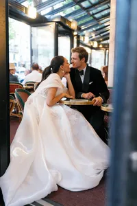 Bride and groom meeting at Café de Flore in Paris, leaning close together and laughing as they touch noses at their table.