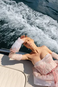 Woman in a blush lace gown reclining on a boat with water spray behind her
