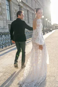 Bride and groom walking through a Paris street lined with lanterns, iron fencing, and historic architecture while holding hands and laughing.