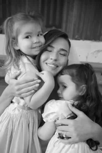 Emotional black-and-white portrait of bride hugging two flower girls before ceremony.