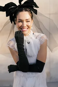 Editorial bridal portrait with a black bow headpiece and long black gloves, laughing
