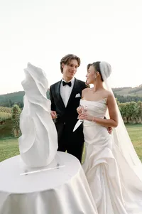 Bride in veil and groom sharing a moment beside architectural wedding cake inspired by her gown.