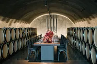 Long rehearsal dinner table styled with deep burgundy florals and elegant glassware and leather table top inside a winery barrel room.