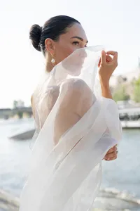 Bridal portrait in Paris featuring a silk veil, pearl earrings, and an elegant updo, captured with the Seine River in the background.