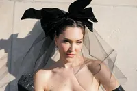 Portrait of a bride in Paris wearing a couture gown, black gloves, and a dramatic bow headpiece with a sheer veil.
