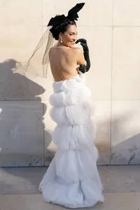 Back portrait of a bride in a couture gown with layered textures, black gloves, and a structured veil headpiece.