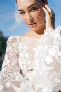 Close portrait of the bride holding her veil while revealing embroidered bird details on her wedding gown.