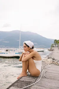 Model sitting on dock by Lake Como in minimal white styling during fashion shoot