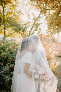 Bride and groom standing in soft sunlight with veil and bouquet in outdoor garden wedding