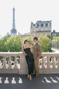 Bride and groom during a morning engagement session in Paris with the Eiffel Tower and historic architecture in the background, the bride wearing a black lace dress with glasses and the groom in a brown suit.